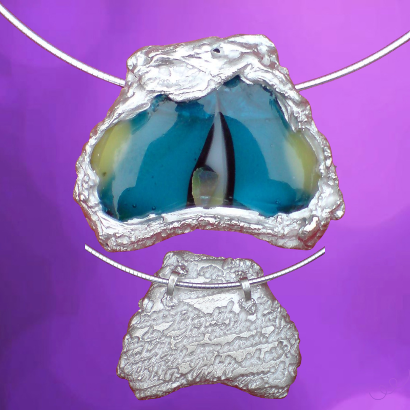 Een stuk glas in verschillende kleuren turkoois en geelgroen met zwart is ingepakt met zilverklei.